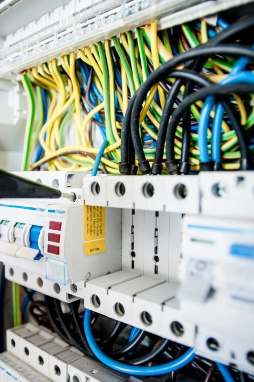 Hand of electrician working on a circuit breaker panel with colorful wires, ensuring safe electrical connections.